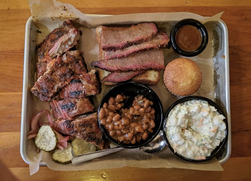 Food truck brisket and pork ribs in a perfect plate of low and slow barbecue with beans, slaw, cornbread, pickles, and sauce.