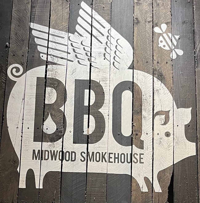 A pig with wings on a wood sign at Charlotte barbecue restaurant Midwood Smokehouse.