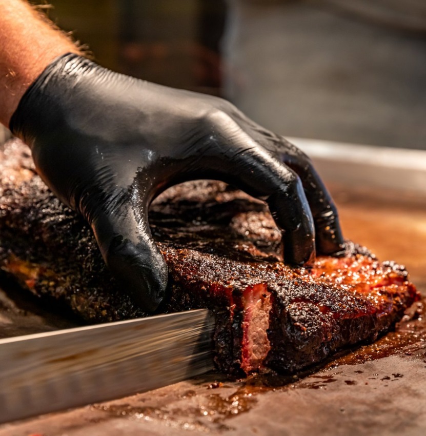 Smoked brisket being sliced on a cutting board.