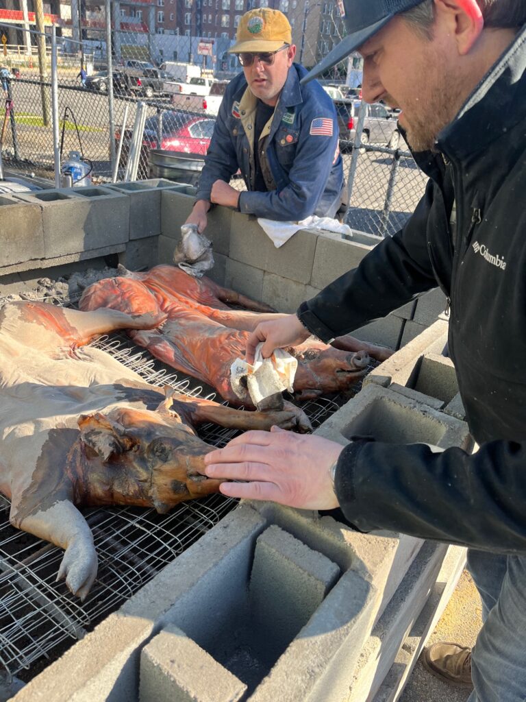 Pitmasters Joel Easton and Elliott Moss wipe ash from a whole hog cooked on a cinder blog pit.