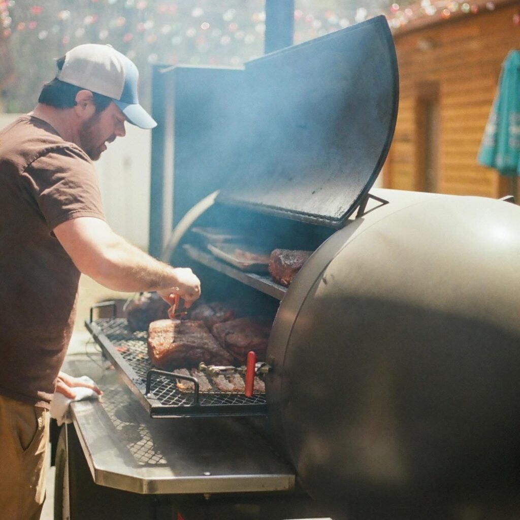 Will checks the meat cooking low and slow in a smoker.